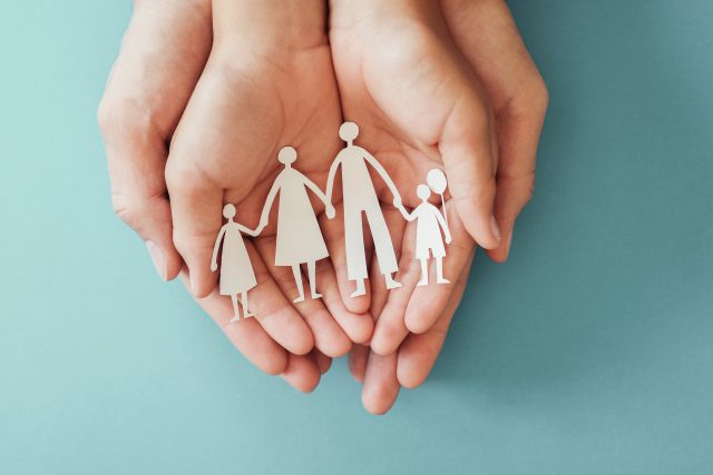 Adult and children hands holding paper family cutout, family hom